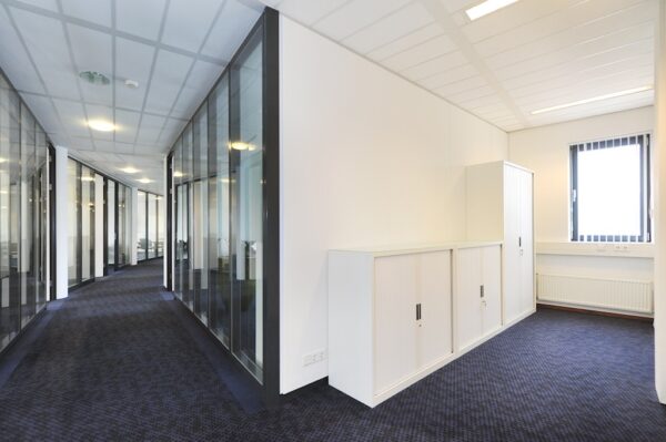 Moderne kantoorruimte aan de Laan van S-Gravenmade met glazen wanden, witte opbergkasten en blauw tapijt.